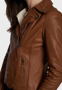 Veste de moto en cuir marron avec une coupe ajustée, fermeture éclair sur le devant et poches latérales. Comprend un col à pression et des détails de couture.