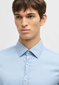 Lichtblauwe shirt met een knoopsluiting, voorzien van een gestructureerde kraag, een gladde textuur en subtiele ribbel-details langs de kraag.