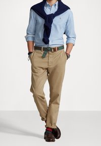 Ljusblå skjorta, khaki chinos, marinblå tröja över axlarna, randigt bälte, bruna loafers och flerfärgade strumpor.