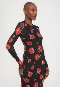 Svart langermet kjole med rødt blomstermønster, tettsittende design og gjennomsiktige detaljer på ermene. Har rund halsutringning og subtil tekstdetalj.