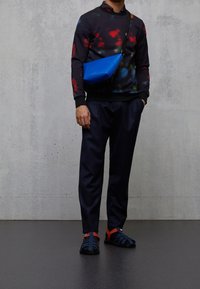 Sudadera negra con patrones de tie-dye coloridos, pantalones navy y bolso cruzado casual azul. Sandalias negras y navy con acentos rojos.