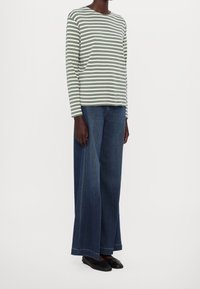 Halenka s dlouhými rukávy, zeleno-bílé pruhované, v kombinaci s džíny modré barvy s vysokým pasem a širokými nohavicemi, a černými balerínkami. Jednoduchý, každodenní outfit.