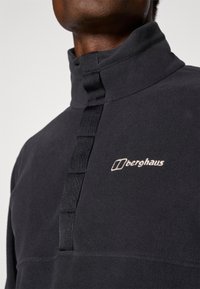 Pullover in pile nero con colletto alto, dotato di zip frontale a mezza lunghezza e logo ricamato. Texture morbida con un design elegante.