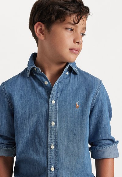 Τζιν πουκάμισο με κουμπιά σε μέτριο μπλε, με μακρυά μανίκια γυρισμένα στους αγκώνες, λευ�κά κουμπιά και ένα μικρό λογότυπο στο στήθος.
