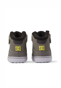 Zapatos DC, grises con detalles en negro, con cuello de forro polar texturizado, suela de goma blanca, presenta el logo en amarillo en los talones y se aseguran con cremalleras.