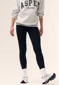 Tumedat lahedad retuusid, millel on sile tekstuur, kokku sobitatud halli dressipluusiga, millel on julge musta kirjaga "ASPEN COLORADO" ning valged tossud.