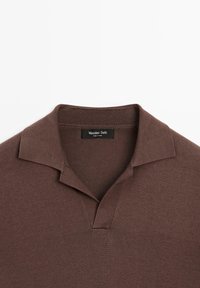 Bruine polo met een zachte textuur, voorzien van een opstaande kraag en een V-hals ontwerp. Het label zegt "Massimo Dutti," wat de oorsprong van het merk aangeeft.