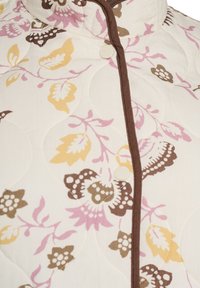Gewatteerd jack in crème met een bloemmotief in roze, geel en bruin. Heeft een opstaande kraag en een bruine bies met knoopsluiting.