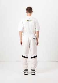 Camiseta blanca de gran tamaño con un logo en la parte posterior, combinada con pantalones blancos de cintura elástica que tienen rayas negras y beige en los tobillos.