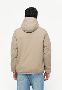 Beige polstret jakke med hætte, der har en glat tekstur og et forsimplet design. Bagudsigten viser en sømdetaille over skuldrene.