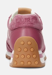 Bakvy av rosa och tan sneakers med gummisula och nitar, samt "Lauren Ralph Lauren" präglat på läderkragen.
