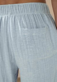 Light blue linen trousers featuring a gathered waistband and a single back pocket. The texture is soft with a subtle, natural weave pattern.