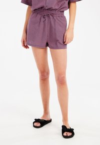 Pantaloni corti a scacchi rossi e bianchi con una fascia elastica in vita e cordino. Abbinati a sandali neri con cinturino a schiocco e dettaglio a fiocco.