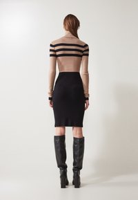 Strickkleid mit einem eng anliegenden schwarzen Rock und einem beigen Oberteil mit horizontalen schwarzen Streifen. Das Model trägt hohe schwarze Lederstiefel.