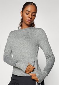 Grå langærmet træningsshirt med en glat tekstur, tætsiddende design, tommelhuller i manchetterne og sideslids for bedre bevægelsesfrihed.