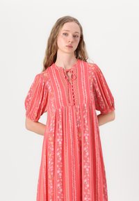 Red floral dress with puff sleeves, tie neck, and button front. Features vertical stripes with intricate floral patterns and a flowing silhouette.