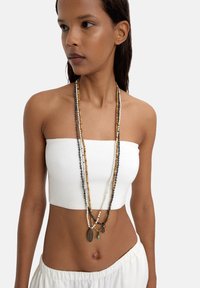 Długa naszyjnik z koralików składa się z wielu wątków w różnych kolorach, w tym kremowym, brązowym i ciemnoszarym, podkreślonym przez małe metalowe charmsy.