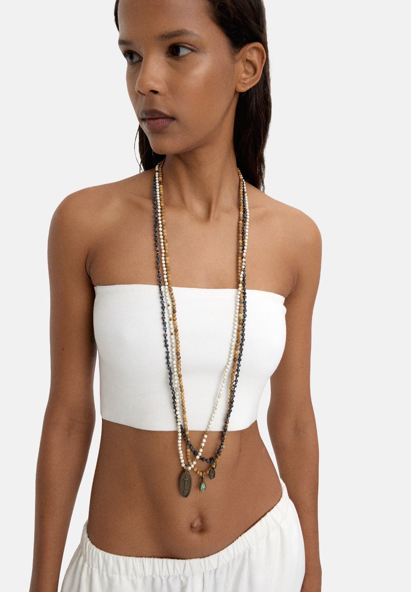 Długa naszyjnik z koralików składa się z wielu wątków w różnych kolorach, w tym kremowym, brązowym i ciemnoszarym, podkreślonym przez małe metalowe charmsy.