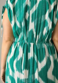 Robe verte et blanche à motifs, avec une taille élastique, des manches courtes avec des liens, et une texture lisse agrémentée d'accents de rayures verticales.