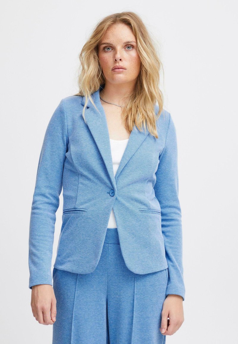 Blazer azzurro chiaro realizzato in materiale morbido, con revers a punta, chiusura a un bottone e due tasche frontali. Dettaglio della superficie texture.