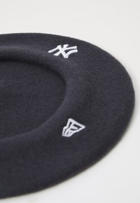 Crni šešir beret s vezanim bijelim NY i F logotipima. Okruglog oblika s teksturiranom površinom i malo uzdignutim rubom.