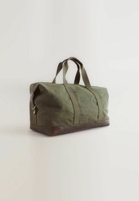 Grøn kanvas duffelbag med brunt læderbund, dobbelte top håndtag og forstærkede syninger. Har lynlåslukning og robuste hardwaredetaljer.