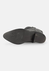 Bota de cuero negra que presenta una punta afilada, parte superior texturizada y una suela plana con ligero desgaste. Presenta un logotipo grabado en la suela.