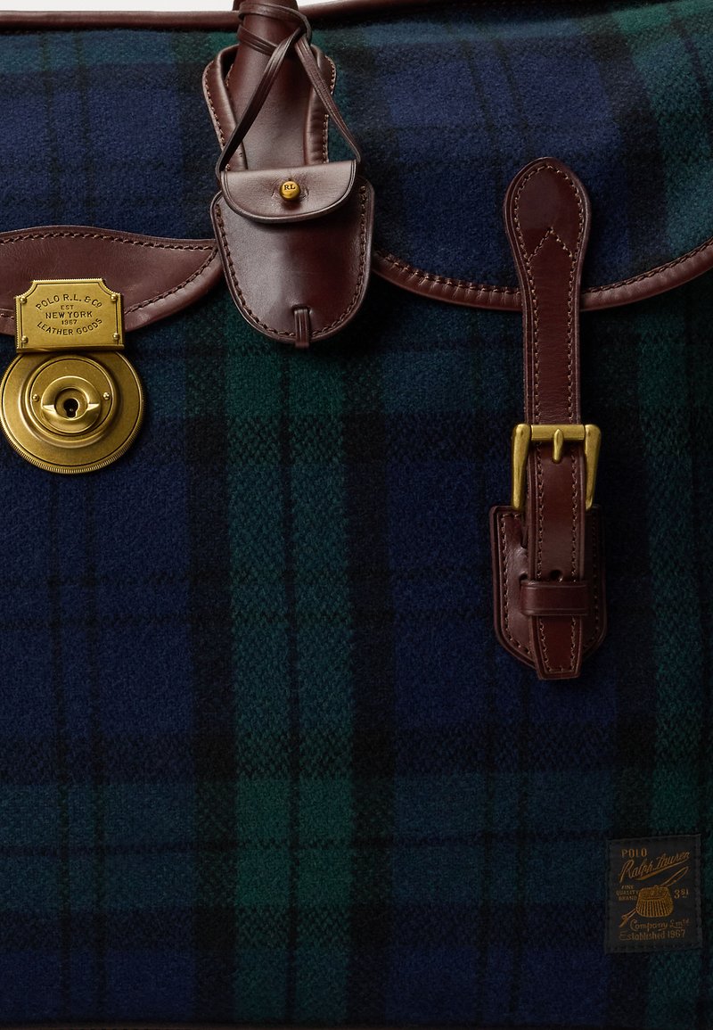 Green and navy plaid wool bag with brown leather accents, brass hardware, and a toggle closure. Features a small leather pouch attached.