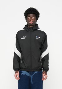 Jachetă neagră cu glugă, decorată cu accente albe, având logo-urile Puma și BMW. Design cu glugă, închidere cu fermoar și manșete elastice.