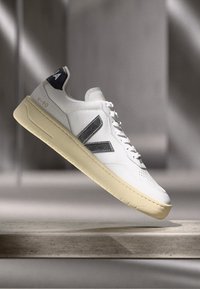 Sneakers bianchi con parte superiore in pelle testurizzata, accenti grigi sui lati e suola in gomma beige. Logo sul tallone.
