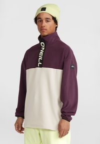 Pullover in pile viola con colletto a mezza zip, presenta una sezione grigio chiaro a contrasto. Logo O'Neill nero sulla zip e sulla manica.