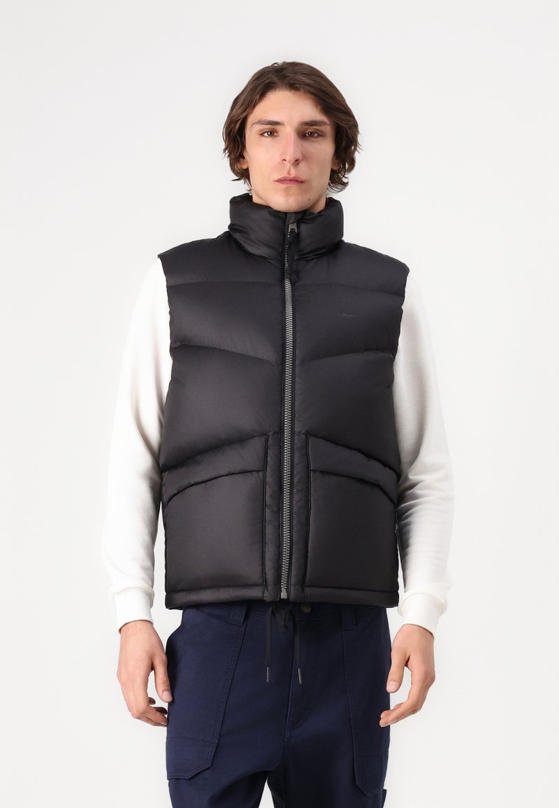 Gilet rembourré noir avec col haut, fermeture zippée et deux grandes poches avant. Le matériau semble lisse et isolé pour la chaleur.