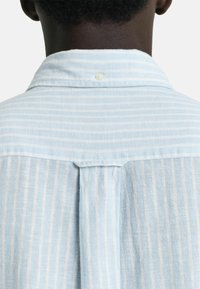 Camicia a righe blu chiaro con colletto button-down, tessuto testurizzato e dettaglio a pieghe sul retro per un design aggiuntivo.