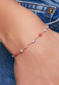 Złota bransoletka łańcuszkowa z wielokolorowymi koralikami w odcieniach różu, fioletu i przezroczystości; gładka tekstura; misternie wykonane detale w kształcie koralików.