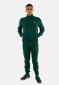 Chándal atlético verde hecho de tejido suave, que incluye una chaqueta con cremallera y pantalones ajustados. Presenta detalles de logotipo en la chaqueta y en los pantalones.
