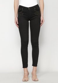 Black skinny jeans made of stretchy fabric, featuring embroidered details on the front pockets. Finished with a zip fly and silver hardware.