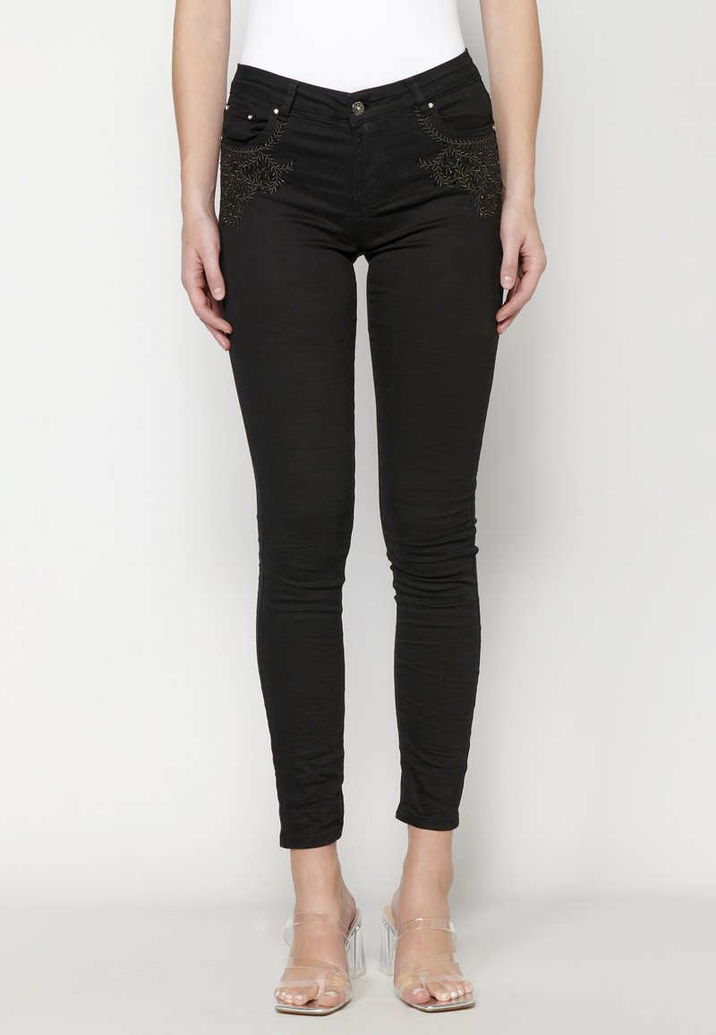 Black skinny jeans made of stretchy fabric, featuring embroidered details on the front pockets. Finished with a zip fly and silver hardware.