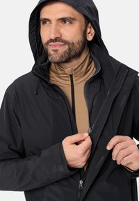 Giacca nera impermeabile con chiusura a zip, cappuccio regolabile e polsini elasticizzati. Lo strato interno presenta un design a collo alto beige.