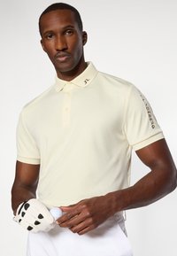 Polo-shirt i lys gul stof, med krave og korte ærmer. Finesser inkluderer et logo på kraven og branding på ærmet.