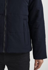 Chaqueta tipo plumas navy con un diseño acolchado, que cuenta con un collar alzado, cremallera frontal y bolsillos laterales. Fabricada con un tejido suave y ligero.
