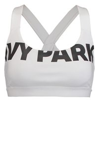 Top sportivo bianco con spalline incrociate e il bold "IVY PARK" in nero sulla fascia del petto.
