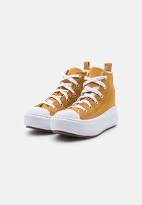 High-top sneakers in mustard yellow canvas, featuring white laces, rubber toe cap, and a thick white platform sole.