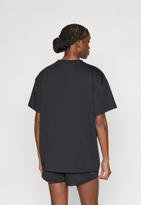 Μεγάλο βαμβακερό μαύρο μπλουζάκι με στρογγυλή λαιμόκοψη και κοντά μανίκια, με απαλή υφή και χαλαρή εφαρμογή, συνδυασμένο με μαύρο σορτς.