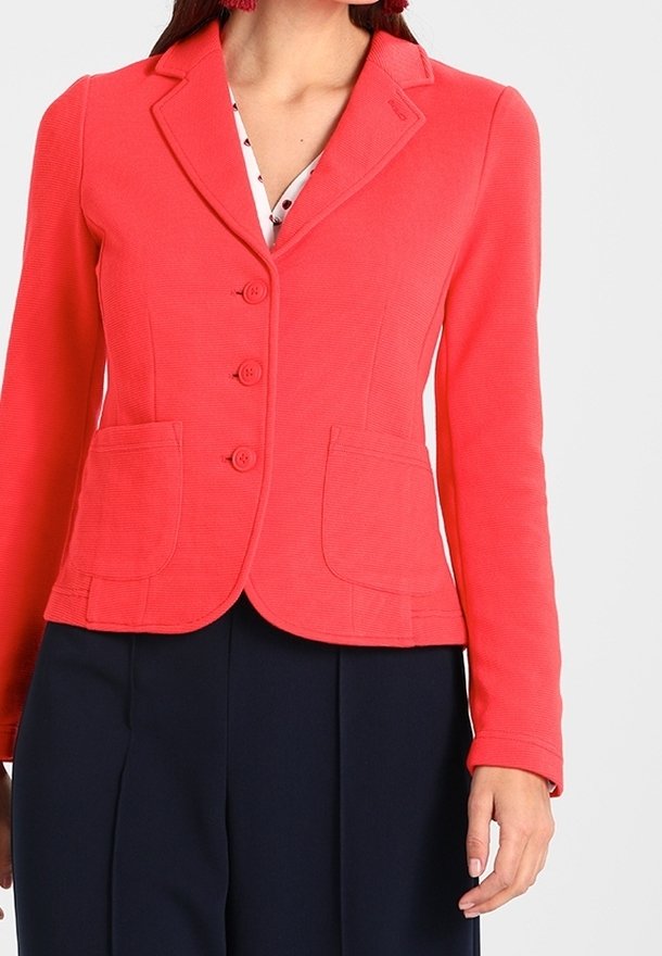 Blazer coral con solapa muestrada, cierre de tres botones y dos bolsillos frontales. Tejido texturizado con un diseño ajustado.
