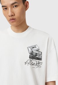 Tricou alb din bumbac, cu un grafic ce reprezintă două casete audio și text scris de mână. Guler rotund și croială lejeră.