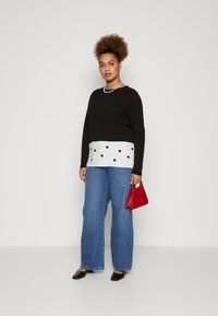 Maglietta nera a maniche lunghe con motivo a pois bianchi nella parte inferiore, abbinata a jeans a gamba larga blu chiaro e con una borsa rossa.