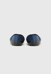 Baskets bleues matelassées à enfiler avec une semelle en caoutchouc noire, présentant une texture lisse et un design minimaliste, une forme arrondie et une languette au talon.