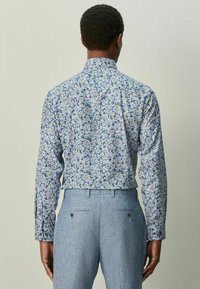 Camisa floral de manga larga con patrones azules y blancos, diseño con cuello y cierre de botones; combinada con pantalones azul claro texturizados.
