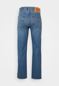 Jeans de ganga azuis com um design de perna reta, apresentando um logo em pele, costura visível e dois bolsos traseiros.