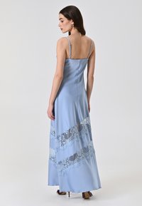 Helles blaues Satin-Maxikleid mit dünnen Trägern, verziert mit Spitzenakzenten entlang des Saums, glatter Textur und taillierter Silhouette.